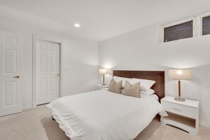 Ein Schlafzimmer mit einem großen Bett, zwei Nachttischen inklusive Lampen, einem Holzkopfende und einem Fenster über dem Bett.