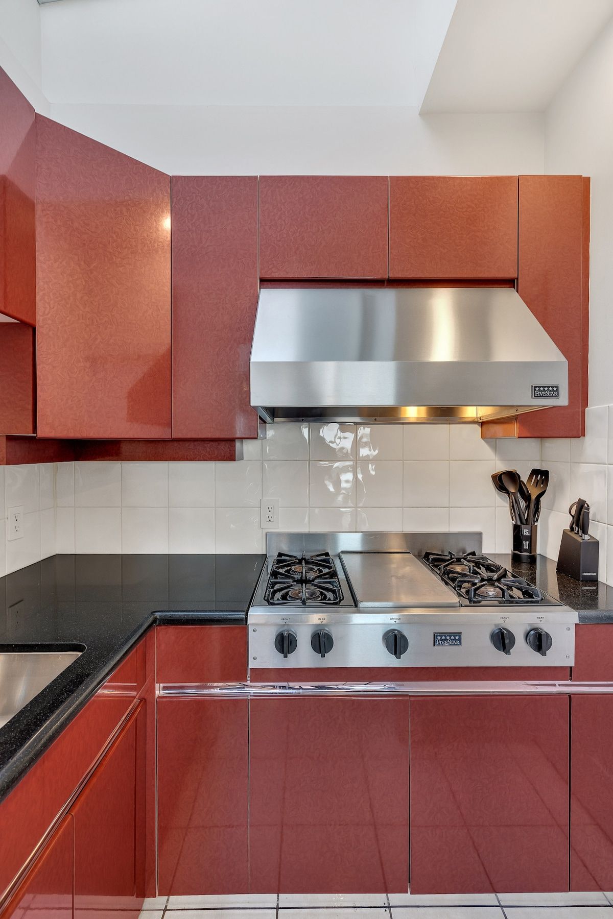 A kitchen with red cabinets, a stainless steel range hood, and a gas stove.
