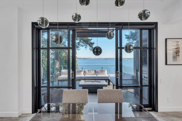 Un comedor moderno con una mesa y sillas de vidrio, vistas al mar a través de amplios ventanales y una decoración minimalista.