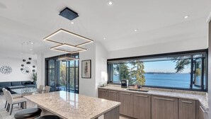 Cozinha moderna com uma ilha grande, área de jantar com mesa de vidro e vista para a água.