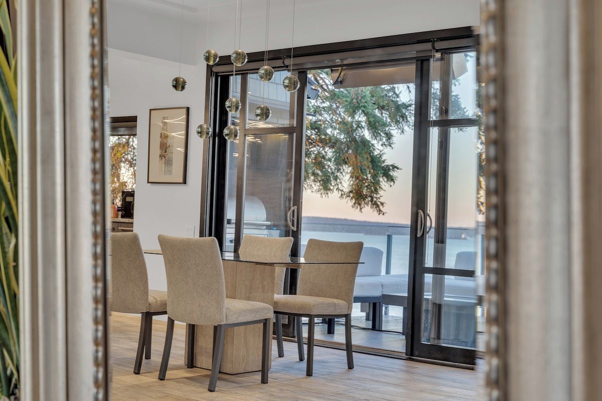 Uma área de refeições com mesa e cadeiras de vidro, uma obra de arte emoldurada na parede e vista através das portas de vidro.