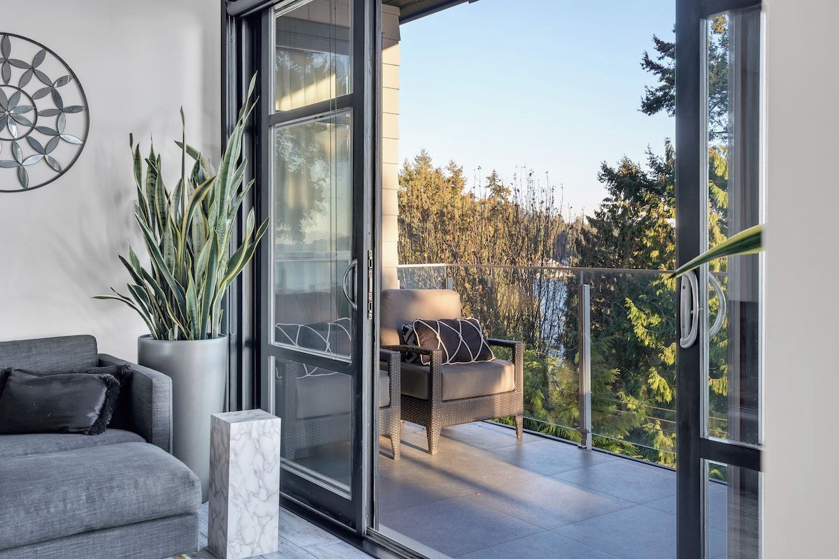 Uma sala de estar moderna com um sofá, uma planta em vaso e uma varanda com vista para árvores.