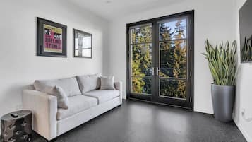 Uma sala de estar moderna com um sofá cinza, uma janela grande com vista para árvores e dois cartazes emoldurados na parede.