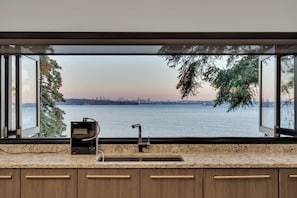 Una cocina con un ventanal que da a una masa de agua y un horizonte urbano distante.