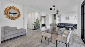 Sala moderna com mesa de jantar de vidro, sofá cinza e espelho grande com moldura em forma de sol.