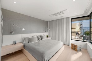 A modern bedroom with a large bed, bedside lamps, a window with a view, and a built-in bench. - Luxe 3BR Beachfront Home | Rooftop Terrace w/ BBQ (Vancouver)