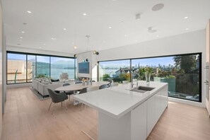 A modern kitchen with a large island, dining area with chairs, and large windows offering a city view. - Luxe 3BR Beachfront Home | Rooftop Terrace w/ BBQ (Vancouver)