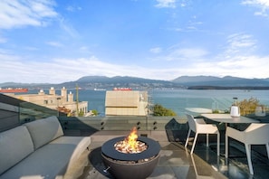 A rooftop terrace with a fire pit, seating area, and a view of a body of water and distant mountains. - Luxe 3BR Beachfront Home | Rooftop Terrace w/ BBQ (Vancouver)