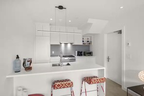 A modern kitchen with white cabinetry, a central island with stools, and a built-in oven. - Luxe 3BR Beachfront Home | Rooftop Terrace w/ BBQ (Vancouver)
