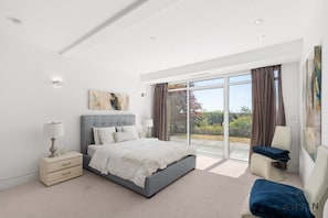 A modern bedroom with a large bed, a nightstand, a chair, and a sliding glass door leading to an outdoor area. - Luxury 5BR Mansion | Pool, Sauna & Scenic Views (West Vancouver)