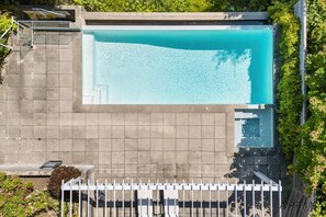 A rooftop pool with a clear blue water surface, surrounded by a white fence and greenery. - Luxury 5BR Mansion | Pool, Sauna & Scenic Views (West Vancouver)