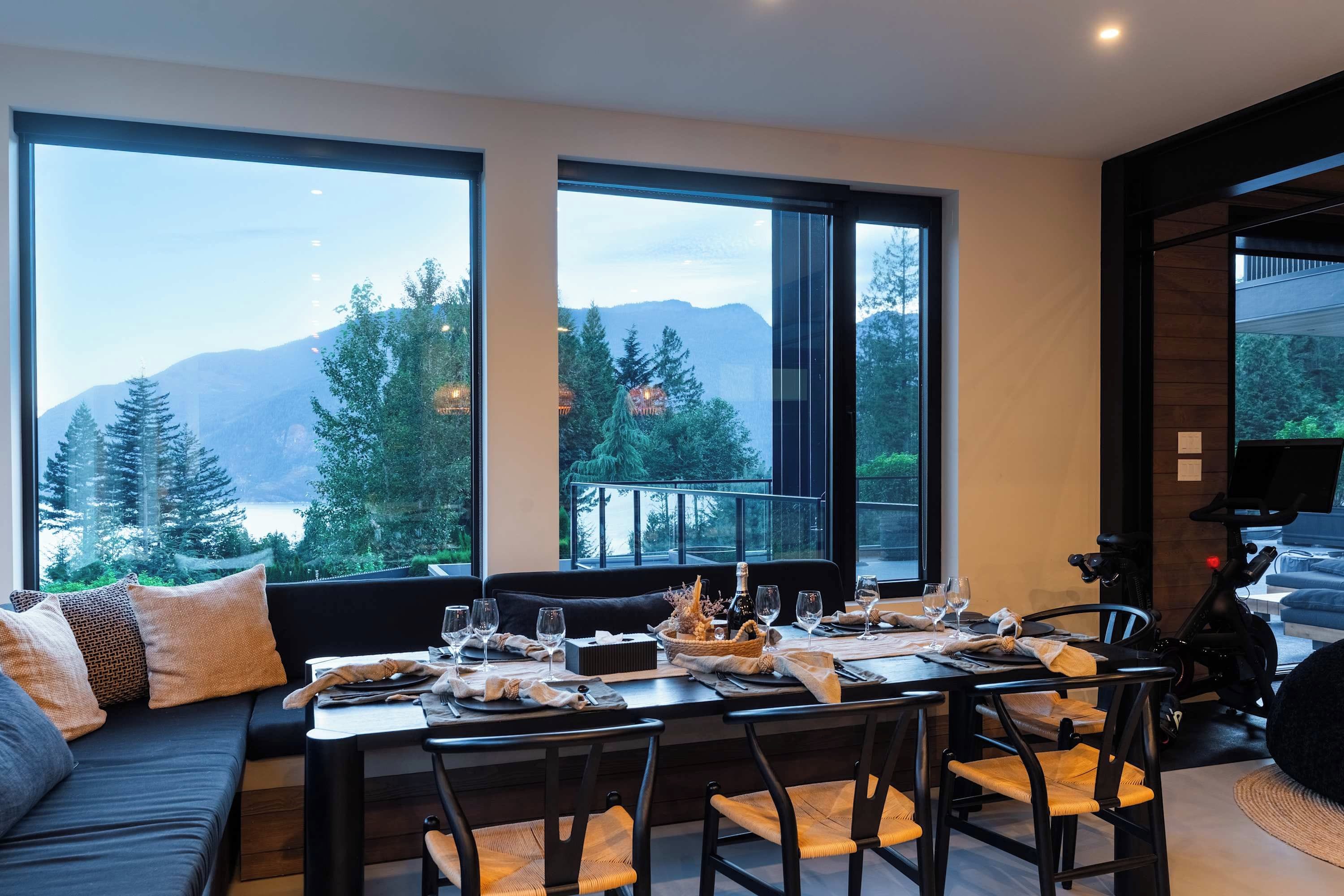 A dining area with a table set for two, large windows offering a mountain view, and a modern interior design.