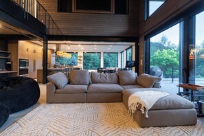 A modern living room with a sectional sofa, a large window, and a view of the outdoors. - 3BR Sea-to-Sky Retreat with Rec Room, Near Creek (Britannia Beach)