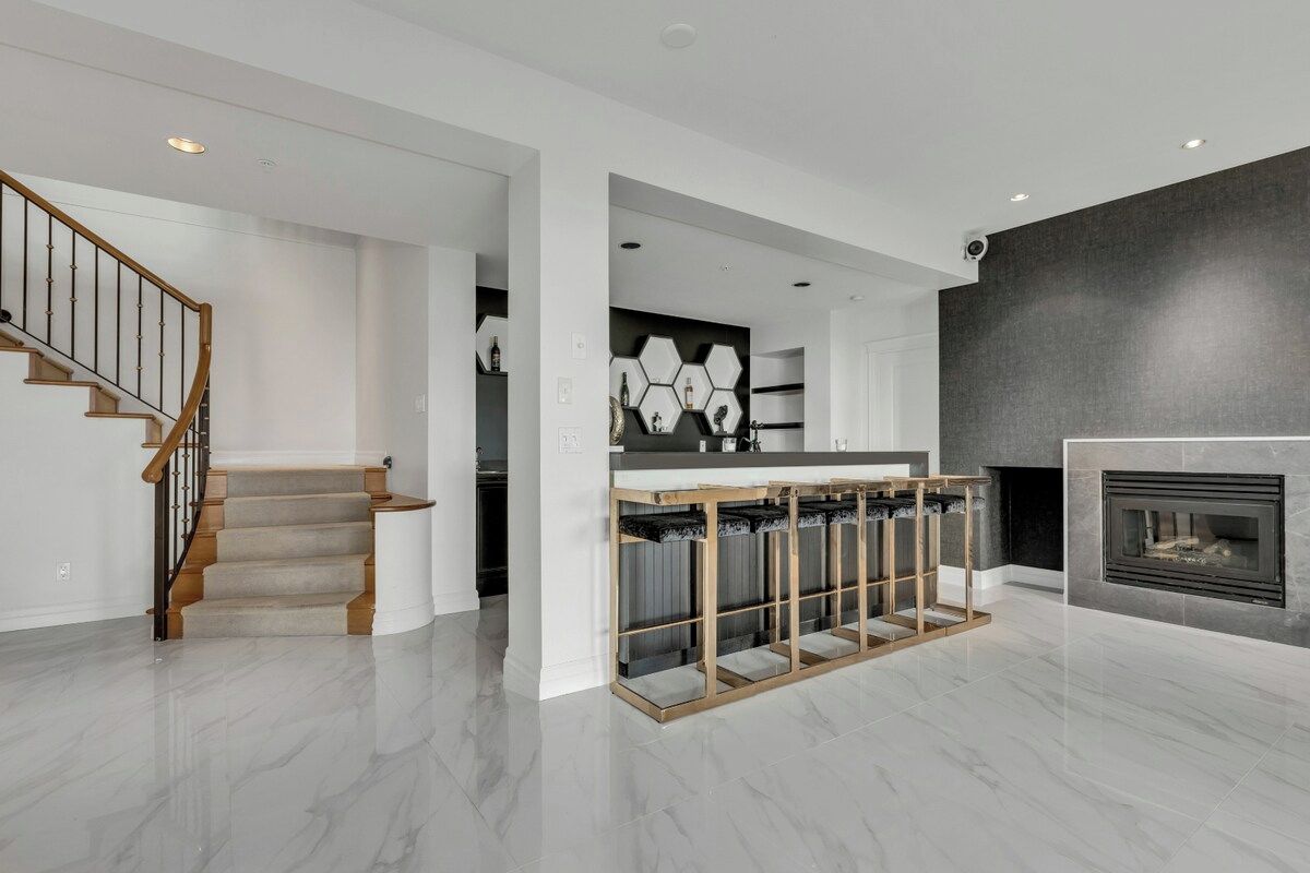 Un intérieur moderne avec un escalier, un coin cuisine doté d’un pare-feu hexagonal et une cheminée.