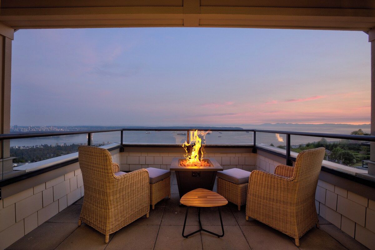 A balcony with wicker furniture, a fire feature, and a view of the cityscape.