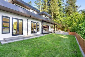 Een modern huis met twee verdiepingen, een overdekte veranda, een verzorgd gazon en een houten omheining.