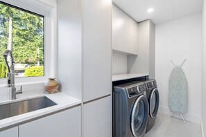 Ein moderner Waschraum mit Waschmaschine, Wäscheständer und einem Fenster mit Blick auf Grünflächen.