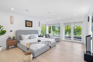 Een moderne slaapkamer met een groot bed, een kleinere zithoek, een televisie en een balkon met uitzicht op groen.