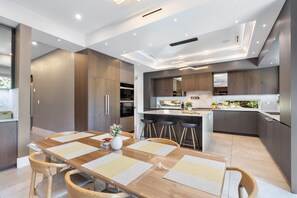 Een moderne keuken met donkerhouten kasten, een centraal eiland met barstoelen, en een eethoek met een houten tafel en stoelen.