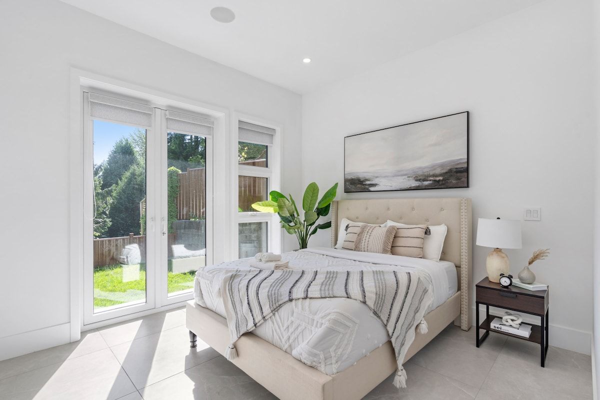A bedroom with a large bed, a nightstand, a wall-mounted lamp, and a painting.