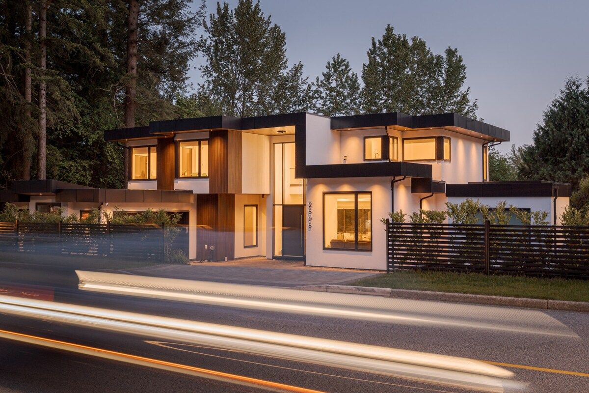 Une maison moderne à deux étages, dotée d’un toit plat, de grandes fenêtres et d’une allée.