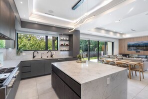 A modern kitchen with a large island, built-in appliances, and a dining area with a view of the outdoors. - Edgemont 5BR Designer Getaway with Home Theater (North Vancouver)