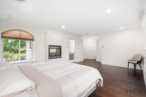 Un dormitorio amplio con una cama grande, una ventana con vistas a vegetación y una puerta que conduce a otra habitación.