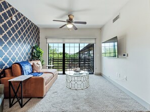 A modern living room with a brown sofa, a glass coffee table, and a ceiling fan. - Cozy 1-bedroom apartment in the historic Bishop Arts area. (Dallas)