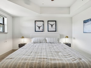 Quarto com uma cama grande, duas luminárias de cabeceira e duas quadros na parede.