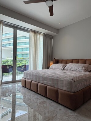 A bedroom with a large bed, a ceiling fan, and a view of a building through a sliding glass door. - Amazing beachfront luxury apartment, brand new, amenities, gym, restaurant. (Nuevo Nayarit)