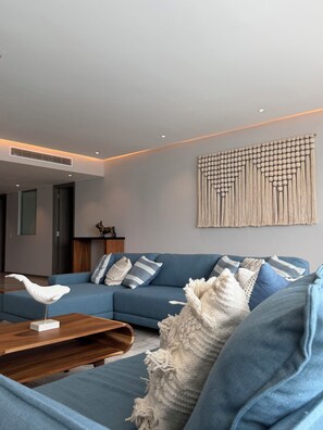 A modern living room with a blue sofa, a wooden coffee table, and a macrame wall hanging. - Amazing beachfront luxury apartment, brand new, amenities, gym, restaurant. (Nuevo Nayarit)