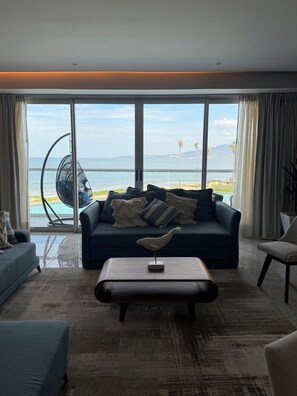 A modern living room with a large window overlooking a beach and ocean. - New 3BR beachfront apartment with incredible view and must see infinity pool. (Nuevo Nayarit)