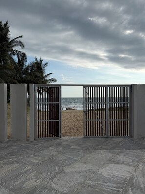 A gated entrance to a beach with a view of the ocean and palm trees. - Amazing beachfront luxury apartment, brand new, amenities, gym, restaurant. (Nuevo Nayarit)