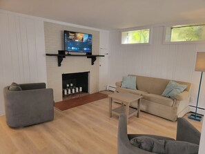 A living room with a fireplace, a television mounted above it, a sofa, a coffee table, and a chair. - Adorable 1-bedroom apartment in lovely Swampscott perfect for getaway (Swampscott)