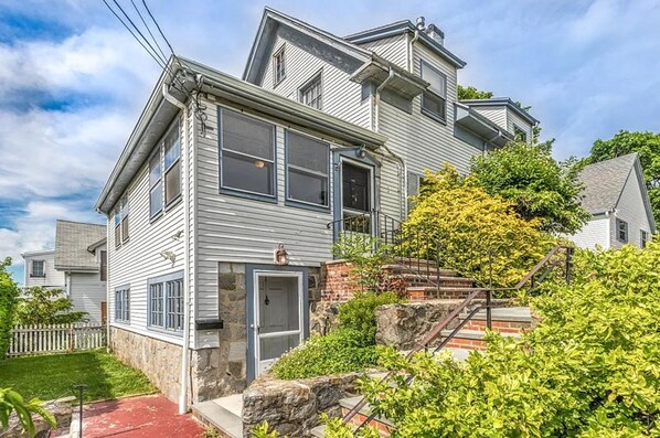 A two-story house with a stone foundation, a front porch, and a staircase leading to the upper level. - Adorable 1-bedroom apartment in lovely Swampscott perfect for getaway (Swampscott)