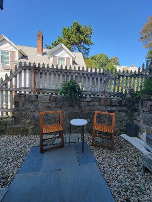 Un patio con dos sillas de madera y una pequeña mesa, rodeado por un muro de piedra y una cerca de madera.