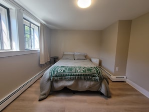 A bedroom with a bed, a bedside table, a heater, and a window with curtains. - Adorable 1-bedroom apartment in lovely Swampscott perfect for getaway (Swampscott)