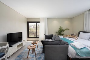 A modern hotel room with a flat-screen TV, a sofa, a bed with a wooden frame, a small table, and a potted plant. - Enjoy at bait assel by spacey #100 (cairo)