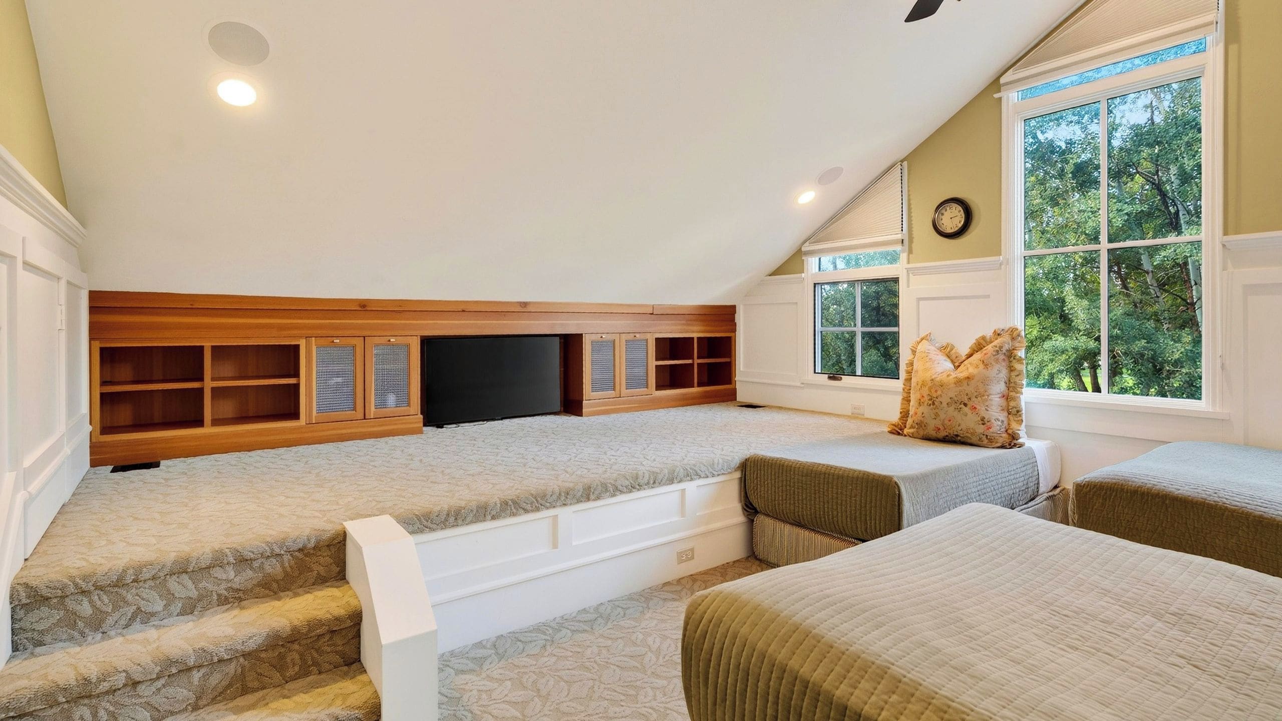 Un dormitorio acogedor en el ático con televisión integrada, estantes de madera y un ventanal con vistas a árboles.