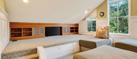 Un dormitorio acogedor en el ático con televisión integrada, estantes de madera y un ventanal con vistas a árboles.