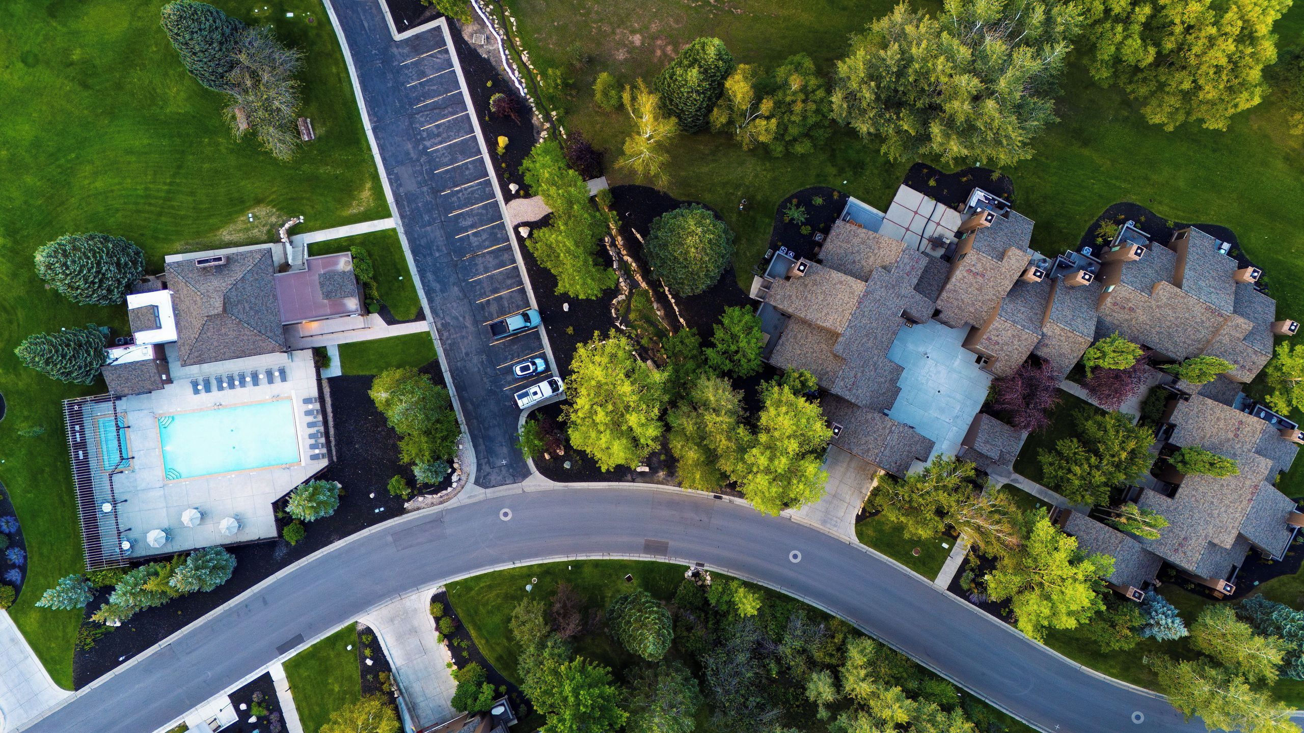 Vista aérea de una zona residencial con piscina, una calle curva y varias casas con diseños de tejados distintos.