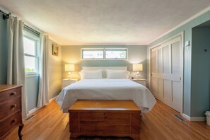 A bedroom with a bed, bedside lamps, a wooden bench, a window, and a door with louvered shutters.