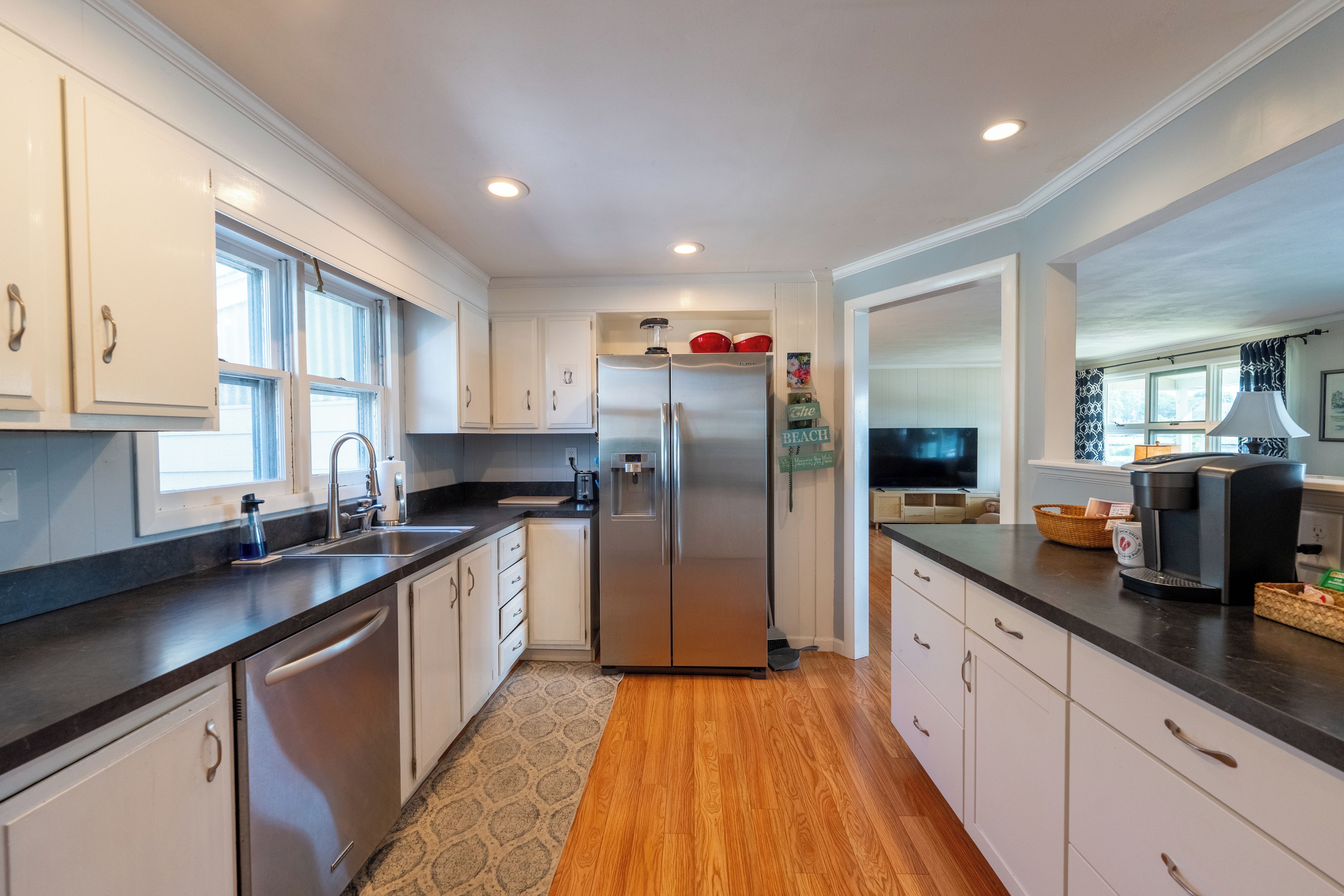 A modern kitchen with white cabinets, a stainless steel refrigerator, a built-in oven, a coffee maker, and a television.