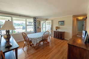 A dining area with a table set for four, wooden chairs, a lamp, and a view of the outside. - Beach House w/ Spacious Yard, Walk to Beach with AC. 10 Minutes to Mystic! (Groton)