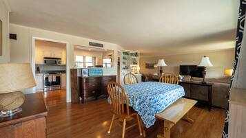 A spacious living area with a dining table, wooden chairs, a sofa, and a television.