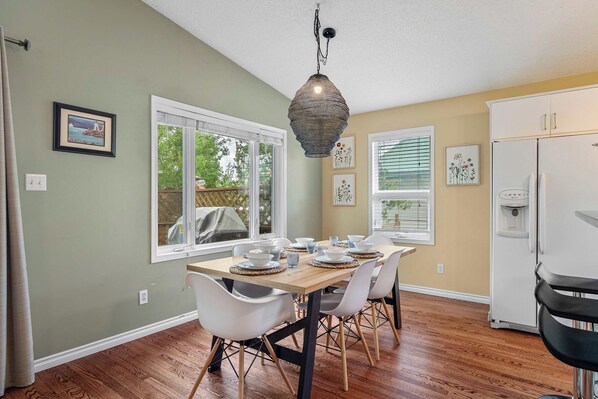 A dining area with a wooden table set for four, white chairs, and a hanging light fixture.