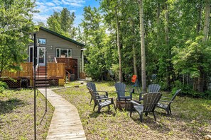 A wooden deck leading to a house with a covered patio, surrounded by trees.