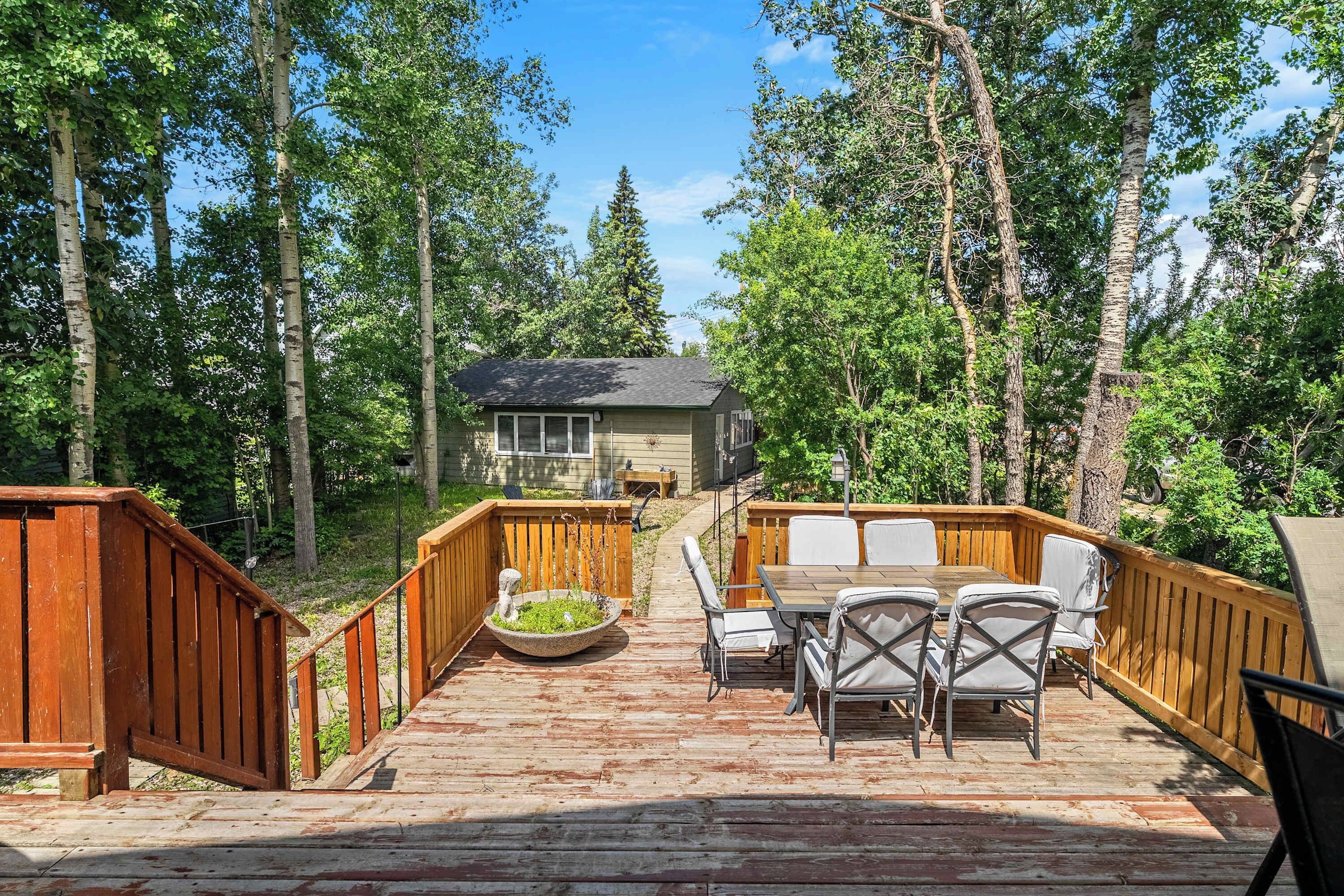 A wooden deck with a table and chairs, surrounded by a forest.