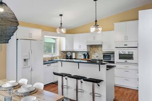 A modern kitchen with white cabinets, a central island with bar stools, a built-in oven, and a wine glass on the counter.