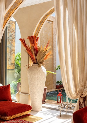 A room with a large vase, red cushions, a small table with candles, and a view of a water feature. - Villa Lenha (Marrakech)